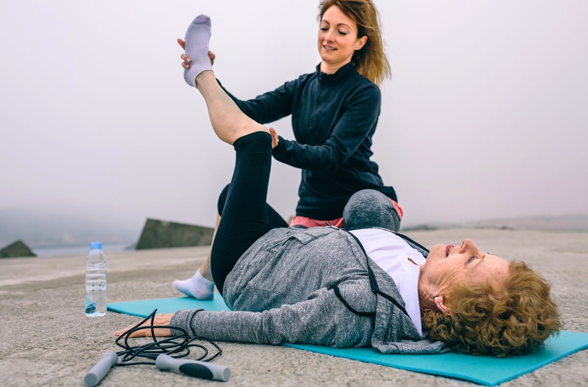 Senior woman with unrecognizable personal trainer stretching leg